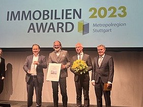 Foto von vier Männern im Anzug die auf einer Bühne stehen. 