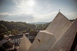  Foto von einer Kirche in einer Stadt, mit Blick von den Dächern der Kirsche. Drumherum ist ein Wald.