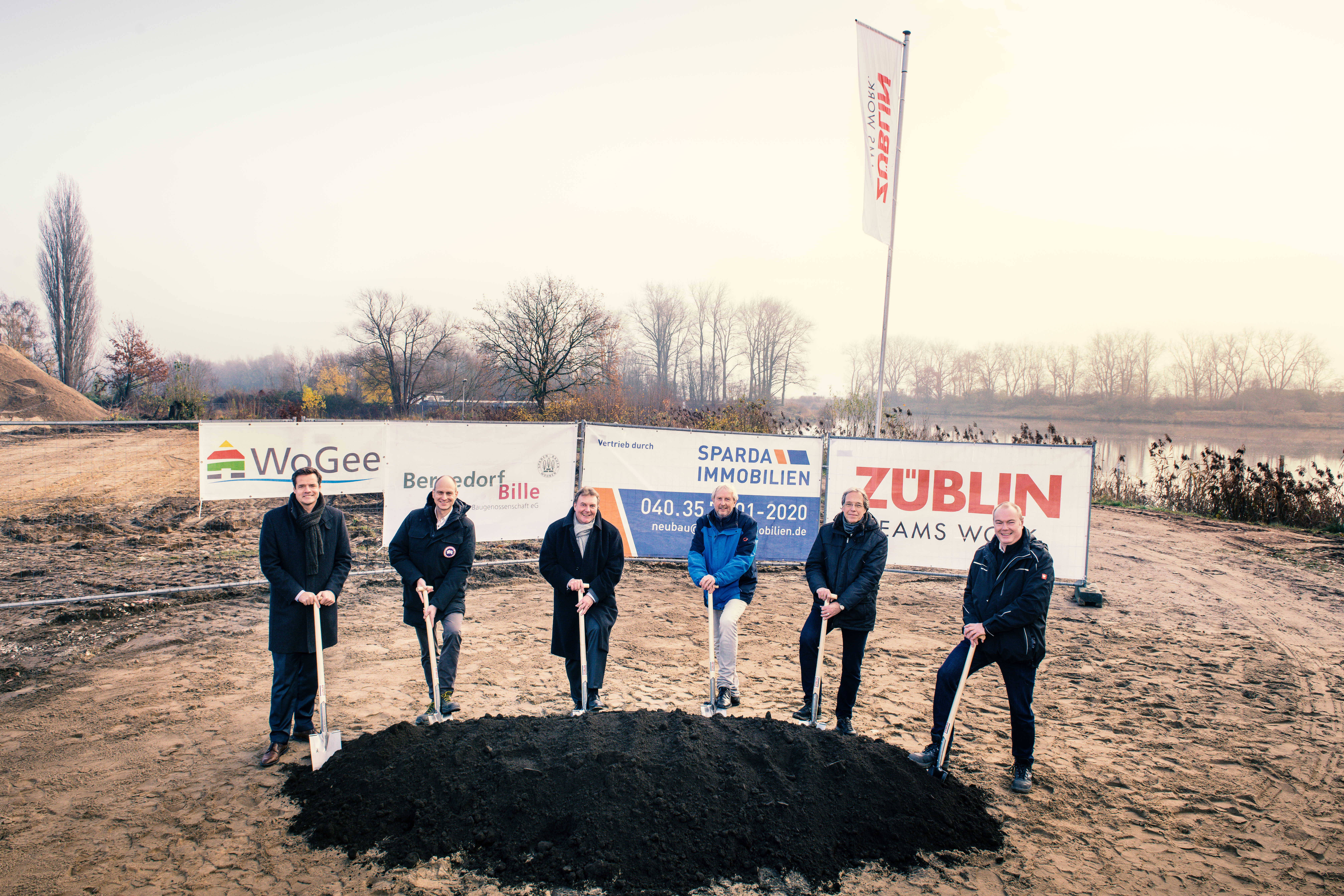 Foto von mehreren Männern, die einem Sparten in die Erde stecken. Sie schauen glücklich. 