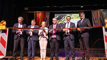 Mehrere Personen schneiden auf einer Bühne ein Band durch