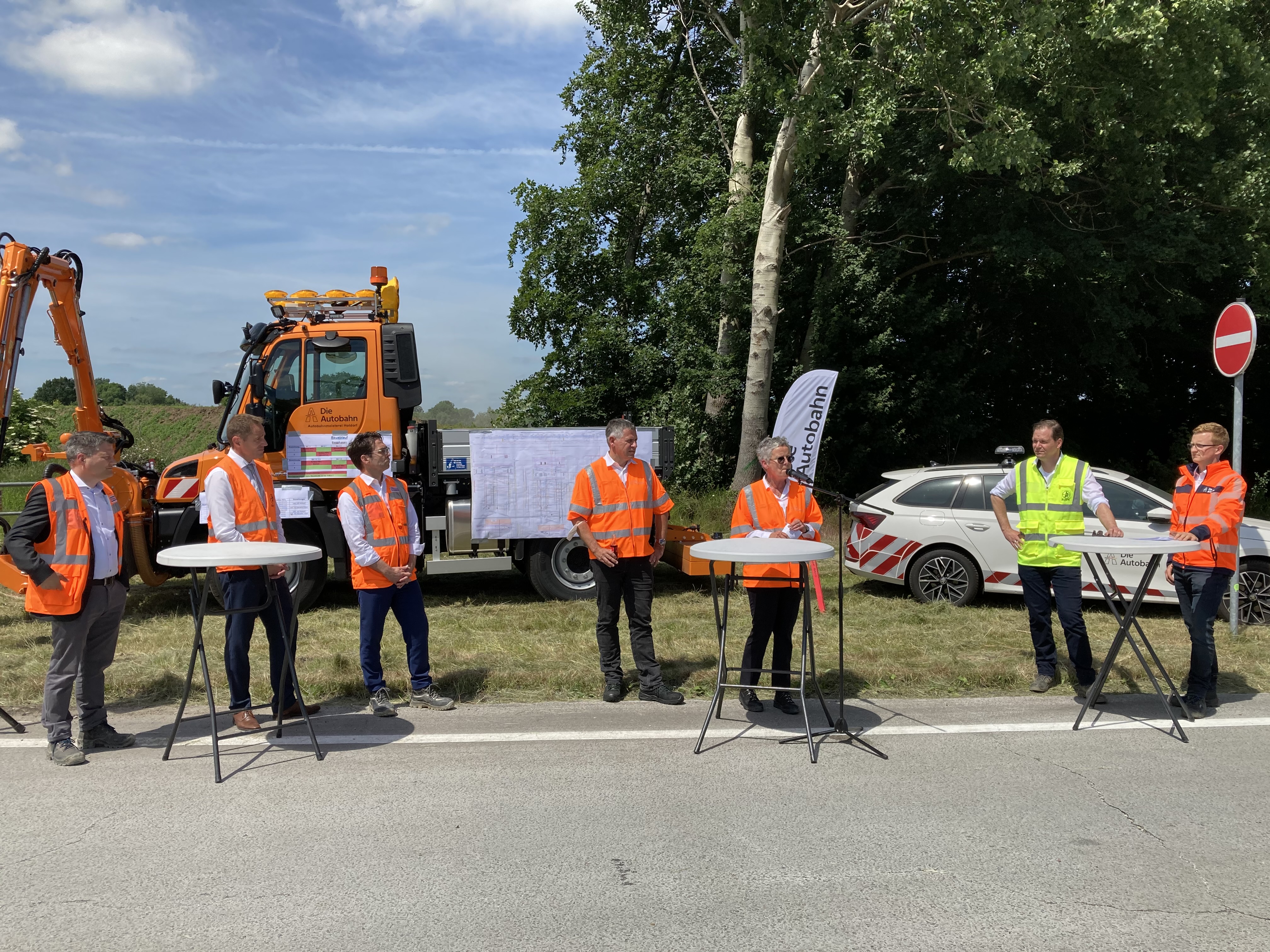 Foto von mehreren Personen in Schutzwesten bei einer Baustellenbesichtigung am Straßenrand stehend