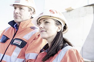 Das Bild zeigt zwei Personen mit weißen Bauhelmen mit der Aufschrift STRABAG