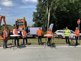 Foto von mehreren Personen in Schutzwesten bei einer Baustellenbesichtigung am Straßenrand stehend