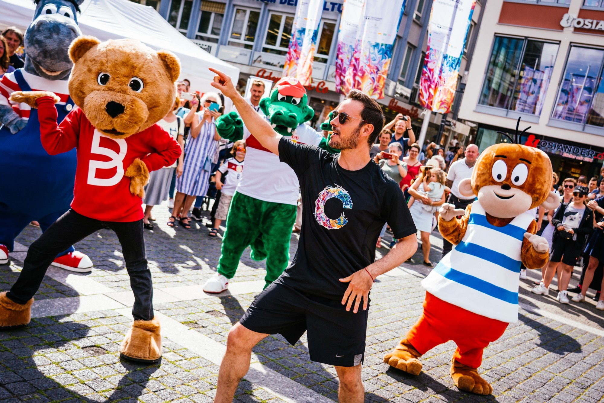 Foto von tanzenden Maskottchen und einem Animator. Drumherum sind viele Menschen.  