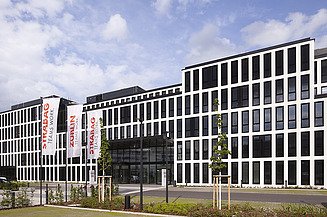Das Foto zeigt das neue Konzernhaus in Köln, ein modernes Gebäude, fünstöckig mit vielen Feinstern, davor eine Grünfläche