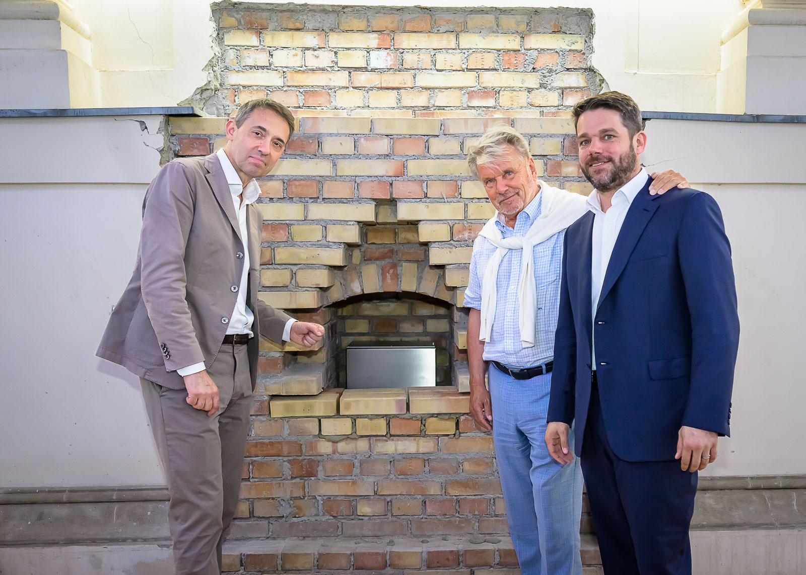 Foto von drei Personen vor einer Ziegelwand bei der symblischen Grundsteinlegung