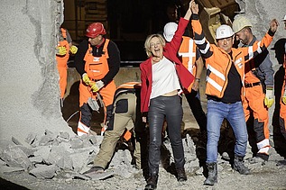 Foto von Personen in Schutzausrüstung und eine schick gekleidete Frau vor einem Tunnel. Die Frau und ein Mann reißen die Arme hoch und freuen sich.  