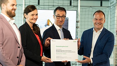 Nahaufnahme von vier Personen die schick gekleidet sind. Sie halten ein Zertifikat. 