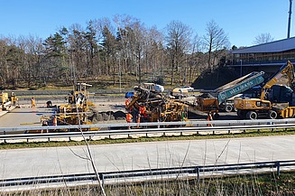 Das Bild zeigt die seitliche Ansicht von mehreren Straßenbaumaschinen beim Einbau einer Betondecke
