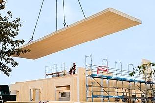 Foto von Neubau am Campus Witten/Herdecke. Ein Kran trägt eine Holzplatte. 