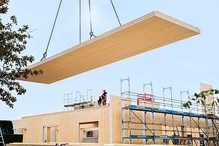 Foto von Neubau am Campus Witten/Herdecke. Ein Kran trägt eine Holzplatte. 