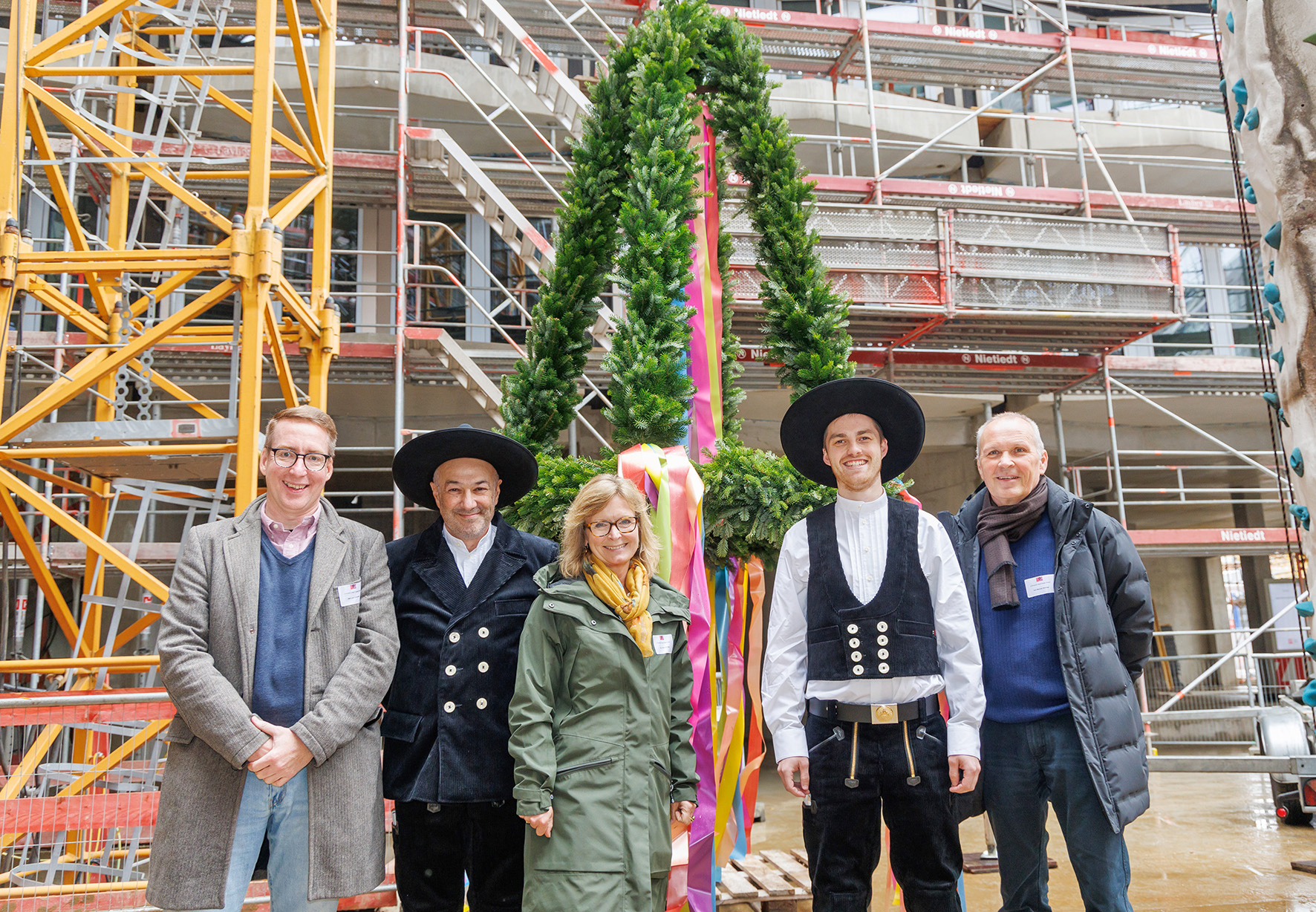 Fünf freundlich schauende Person stehen vor einem Richtkranz  