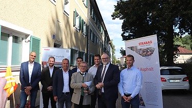 Foto von mehreren Personen, die vor einem gelben Gebäude stehen, hinter ihnen sind zwei Roll-ups