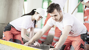 Das Bild zeigt zwei Personen in Arbeitskleidung bei der Arbeit