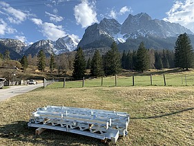 Foto von Stahlelementen die auf einer Wise vor einem Gebirge liegen.   