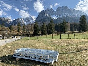 Foto von Stahlelementen die auf einer Wise vor einem Gebirge liegen.   
