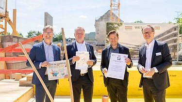 Foto von vier Männern in Anzug auf einer Baustelle. Sie schauen freundlich. 