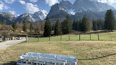 Foto von Stahlelementen die auf einer Wise vor einem Gebirge liegen.   