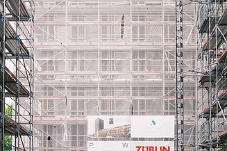 Foto von mehren Personen auf einer Baustelle. Auf einem Gerüst wird der Richtspruch verkündet. 