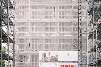 Foto von mehren Personen auf einer Baustelle. Auf einem Gerüst wird der Richtspruch verkündet. 