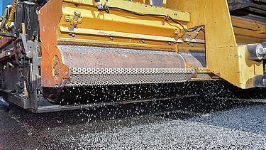 Foto einer Detailansicht einer gelben Asphaltiermaschine bei der Arbeit