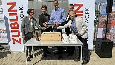 Foto von mehreren Personen, die eine Röhre halten bei der Grundsteinlegung.  