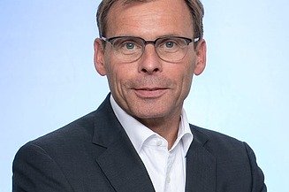 Portrait von einem Mann im Anzug mit Brille. 