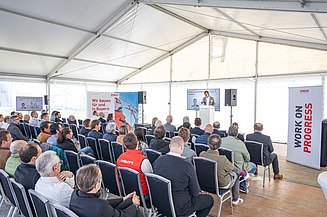 Ein Mann steht auf eine Bühne. Vor der Bühne sitzen die Zuhörer