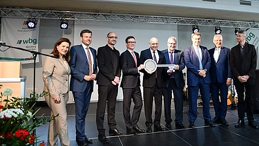 Foto von mehreren Personen, die auf einer Bühne stehen und einen Schlüssel halten. 