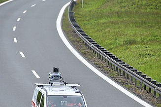 Foto eines Fahrzeuges mit einem Vermessungsgerät auf dem Dach auf einer zweispurigen Fahrbahn