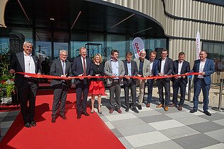 Bild von mehreren Persoen, die ein rotes Band durchschneiden