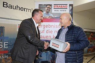 Foto von zwei Personen, die sich die rechte Hand schüttel, die Person rechts hält eine Geldschatulle in der linken hand