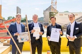 Foto von vier Männern in Anzug auf einer Baustelle. Sie schauen freundlich. 
