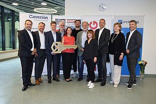 Foto von mehreren Personen bei der Schlüsselübergabe, sie stehen vor zwei Roll-ups