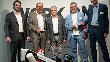 Foto von mehreren Personen, die hinter einen Roboterhund stehen. 