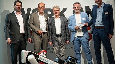 Foto von mehreren Personen, die hinter einen Roboterhund stehen. 