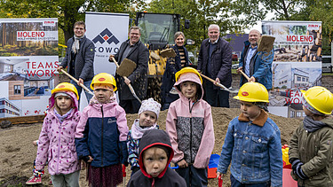 Foto vom symbolischen Spartenstich. Im Hintergrund sind mehrere Personen im Anzug zusehen. Im Vordergrund stehen Kinder, die einen Helm anhaben. 
