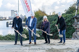 Foto von vier Personen mit Schaufeln, die einen Spatenstich durchführen, dahinter ein STRABAG Segelbanner