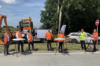 Foto von mehreren Personen in Schutzwesten bei einer Baustellenbesichtigung am Straßenrand stehend