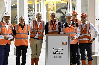Foto von mehreren Personen in Schutzausrüstung die vor einem Rednerpult stehen. 