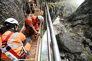 Foto von zwei Personen in Schutzuniform die in einer Schlucht an einer kleinen Brücke schrauben.    