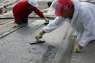  Foto von zwei Personen die mit Spachteln ein Gitter mit Beton bestreichen.