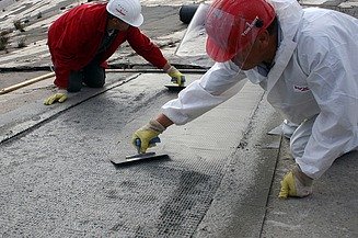  Foto von zwei Personen die mit Spachteln ein Gitter mit Beton bestreichen.