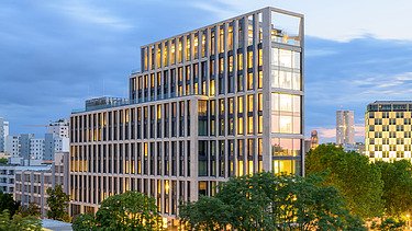 Breites Hochhaus hinter grünen Bäumen