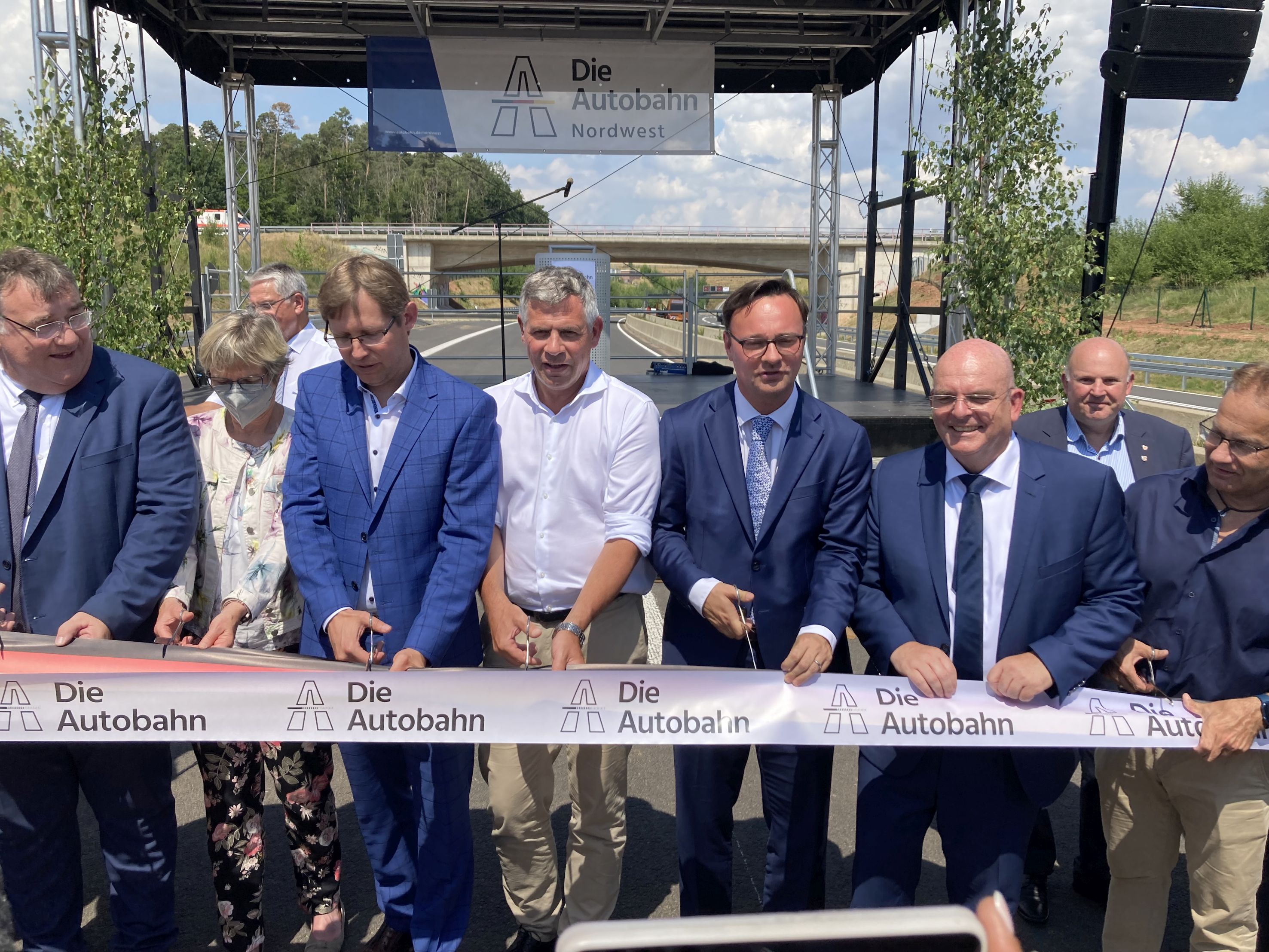 Foto von der feierlichen Verkehrsfreigabe, mehrere Personen durchschneiden ein dickes Band