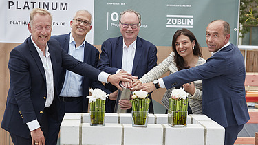 Foto von mehreren Personen, die ihre auf eine Röhre legen zur Grundsteinlegung.   