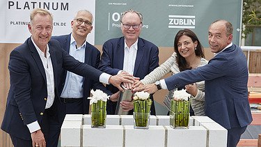 Foto von mehreren Personen, die ihre auf eine Röhre legen zur Grundsteinlegung.   