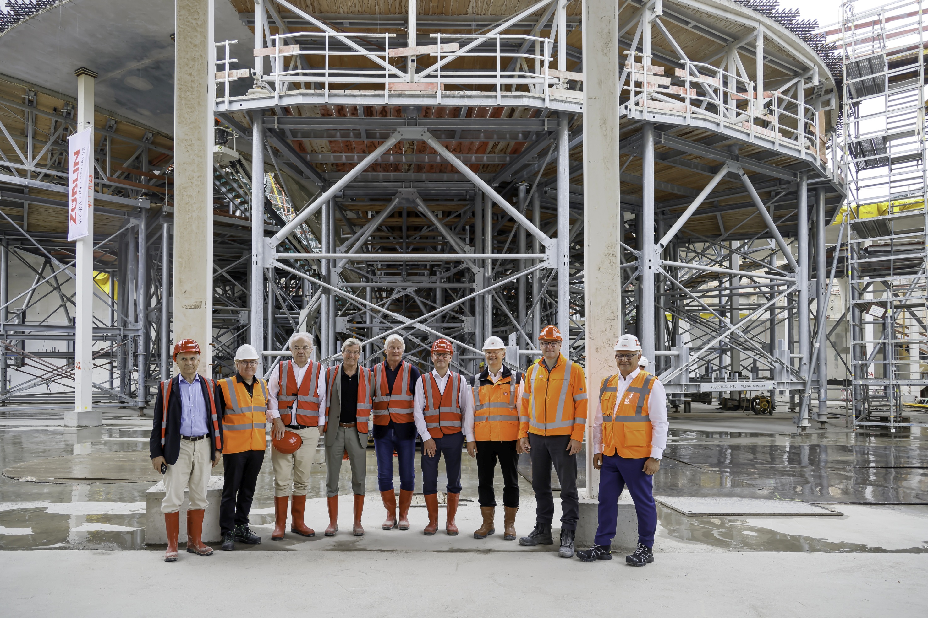 Foto von mehreren Personen, vor einem Gerüst, in Schutzausrüstung. 