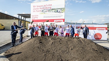 The picture shows several people behind a pile of earth at the symbolic ground-breaking ceremony