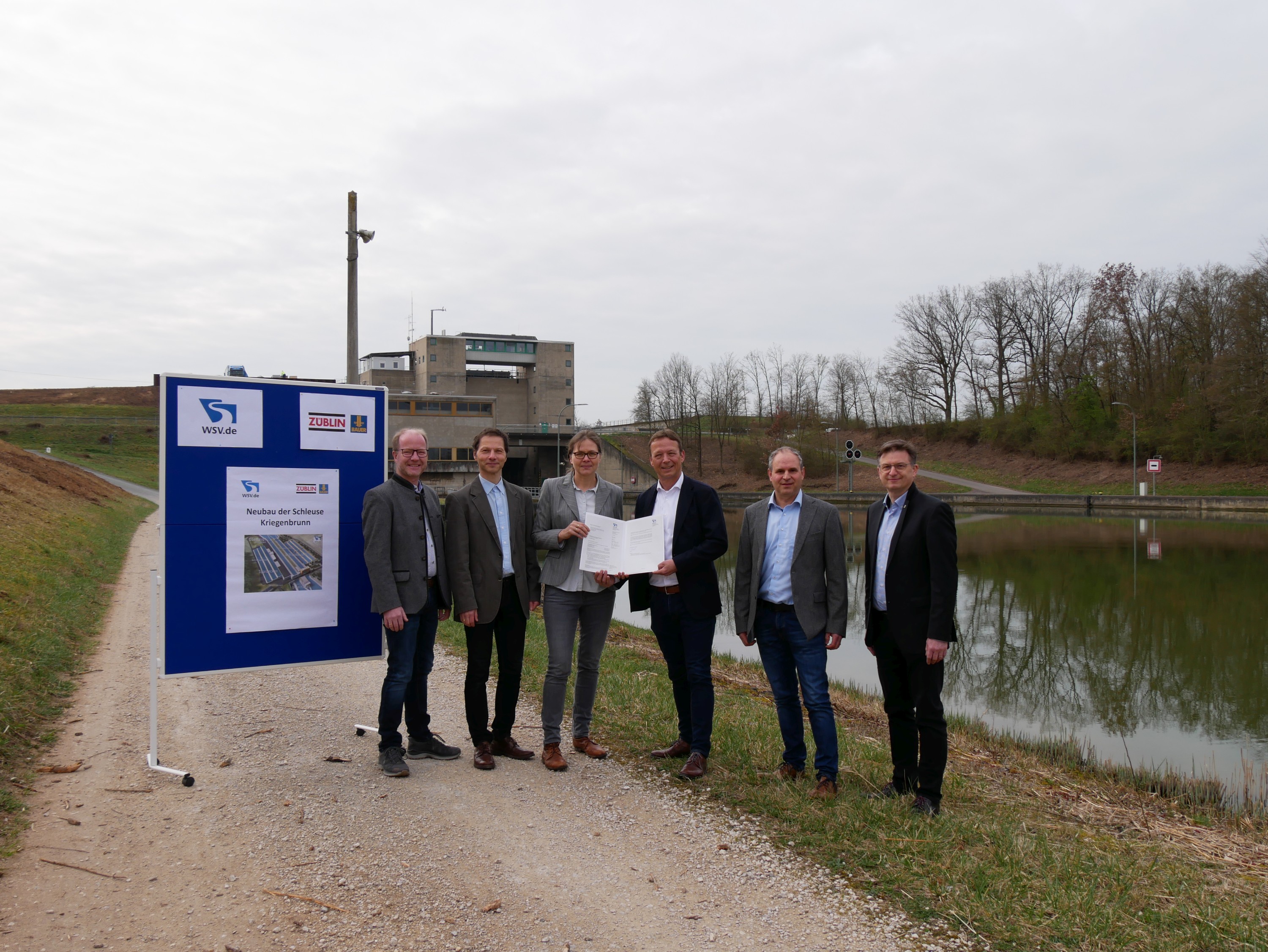 Photo of five people standing on a gravel road, to the left a blue sign